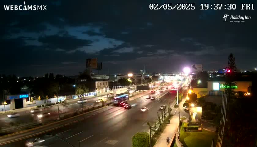 A nighttime view of a multi-lane highway with moderate traffic under a partly cloudy sky.