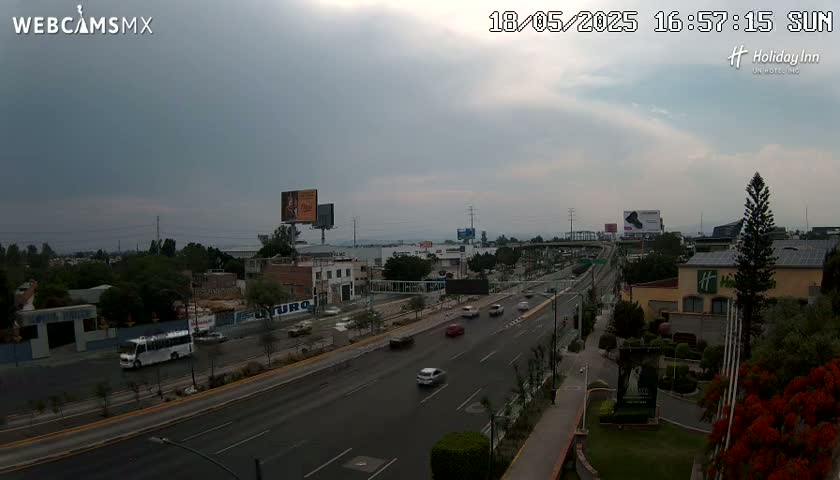A multi-lane highway with moderate traffic flows through a city under an overcast sky.