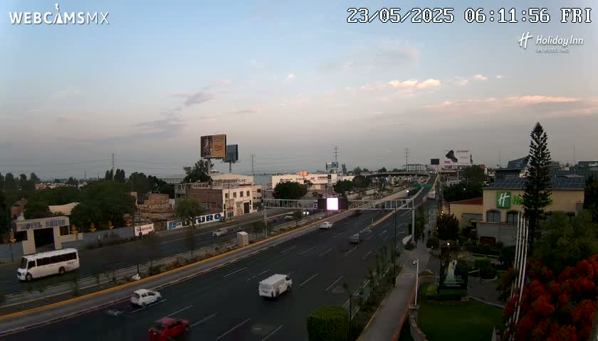 A multi-lane highway with light traffic is shown under a partly cloudy twilight sky.