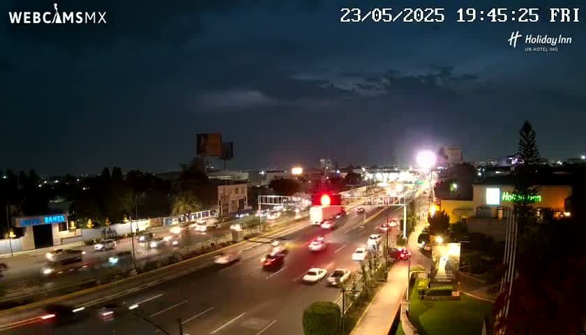 A nighttime view of a multi-lane highway with moderate traffic under a partly cloudy sky.
