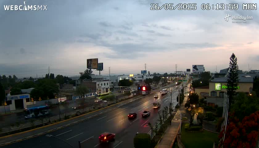 A wet, multi-lane highway with cars driving in both directions under a cloudy, twilight sky.