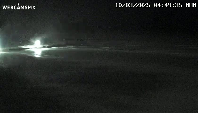 A nighttime long shot shows a dark, flat expanse of land reflecting a bright light source in the distance under a clear sky.
