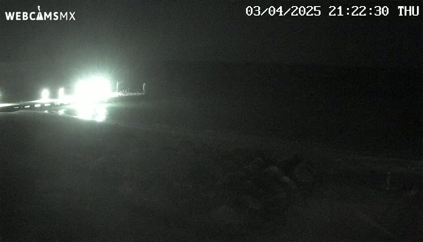 A nighttime, dimly lit view of a roadway and what appears to be a pier or similar structure, with bright lights illuminating the area.