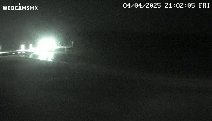 A nighttime view of a highway with vehicle headlights visible in the distance under dark conditions.