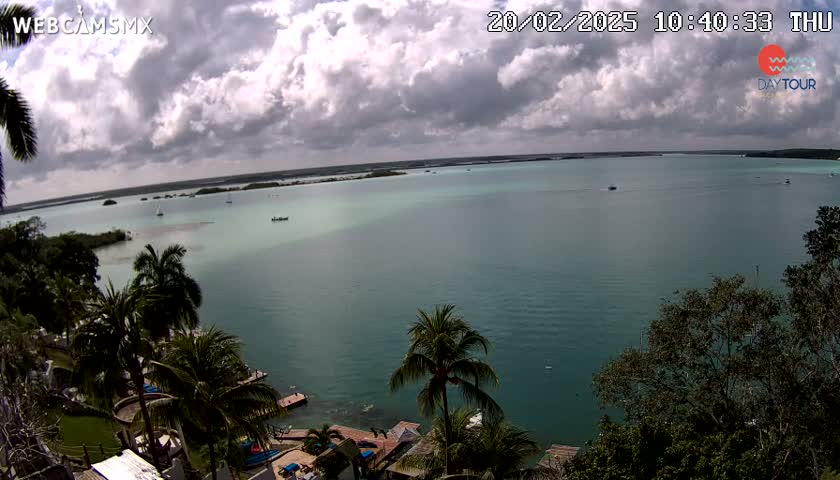 A partly cloudy day overlooks a teal-colored body of water dotted with small boats, surrounded by lush green vegetation.