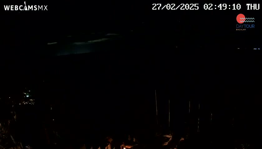 A dark nighttime scene shows a faint, bright horizon line above a mostly black landscape with a few faint lights visible in the lower portion.