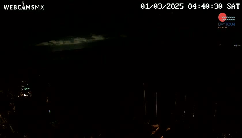 A nighttime, mostly dark scene shows a few faint lights in the distance and a thin layer of clouds in the dark sky.