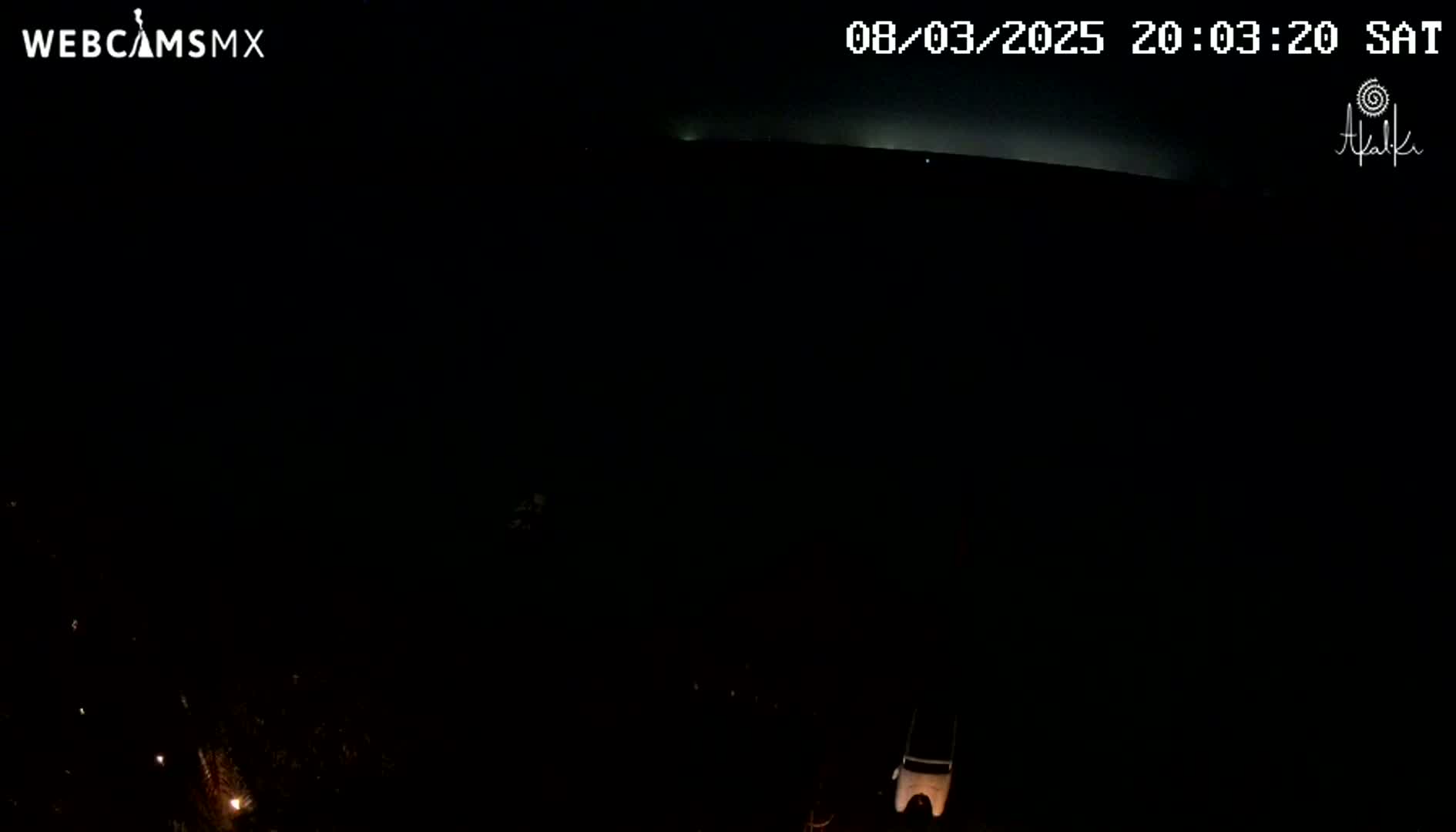 A nighttime, dark scene shows a faintly illuminated horizon line under a mostly clear sky.