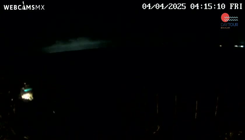 A nighttime, dark scene shows faint light sources in the distance under a cloudy sky.