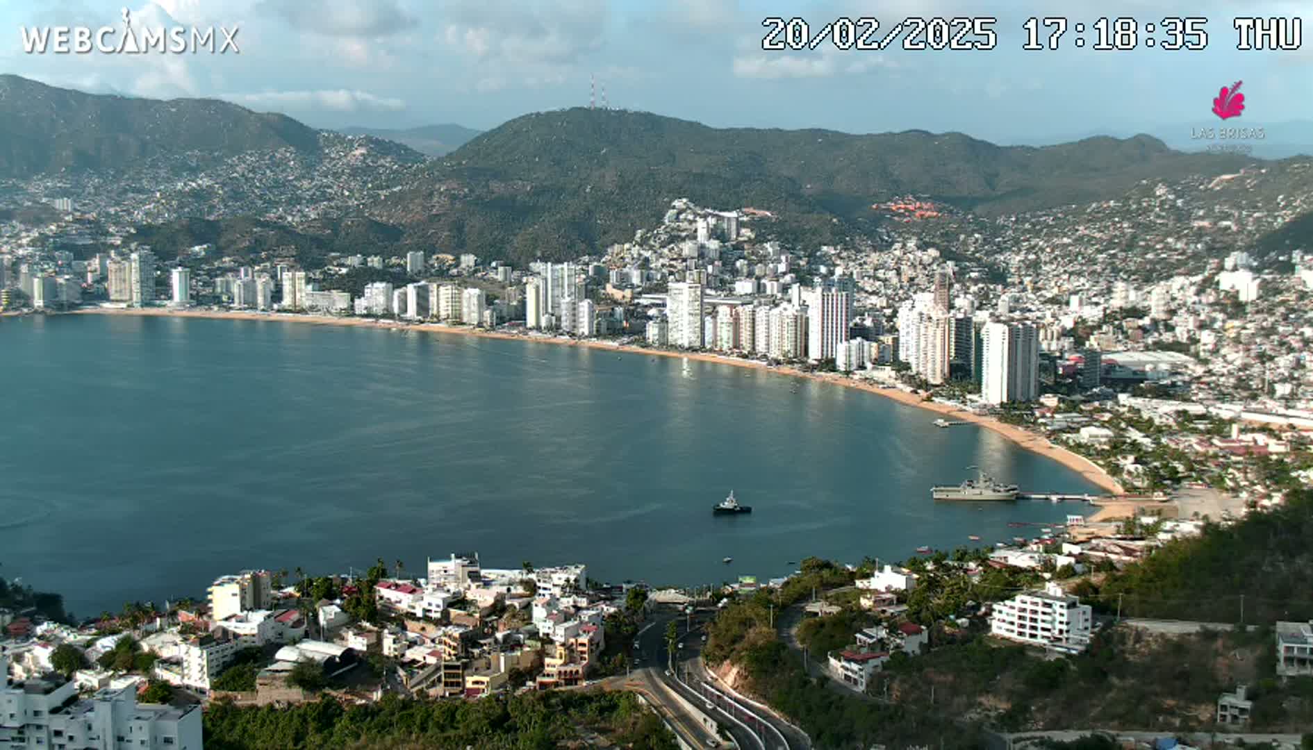 A coastal city with high-rise buildings curves along a sandy beach and bay under partly cloudy skies.