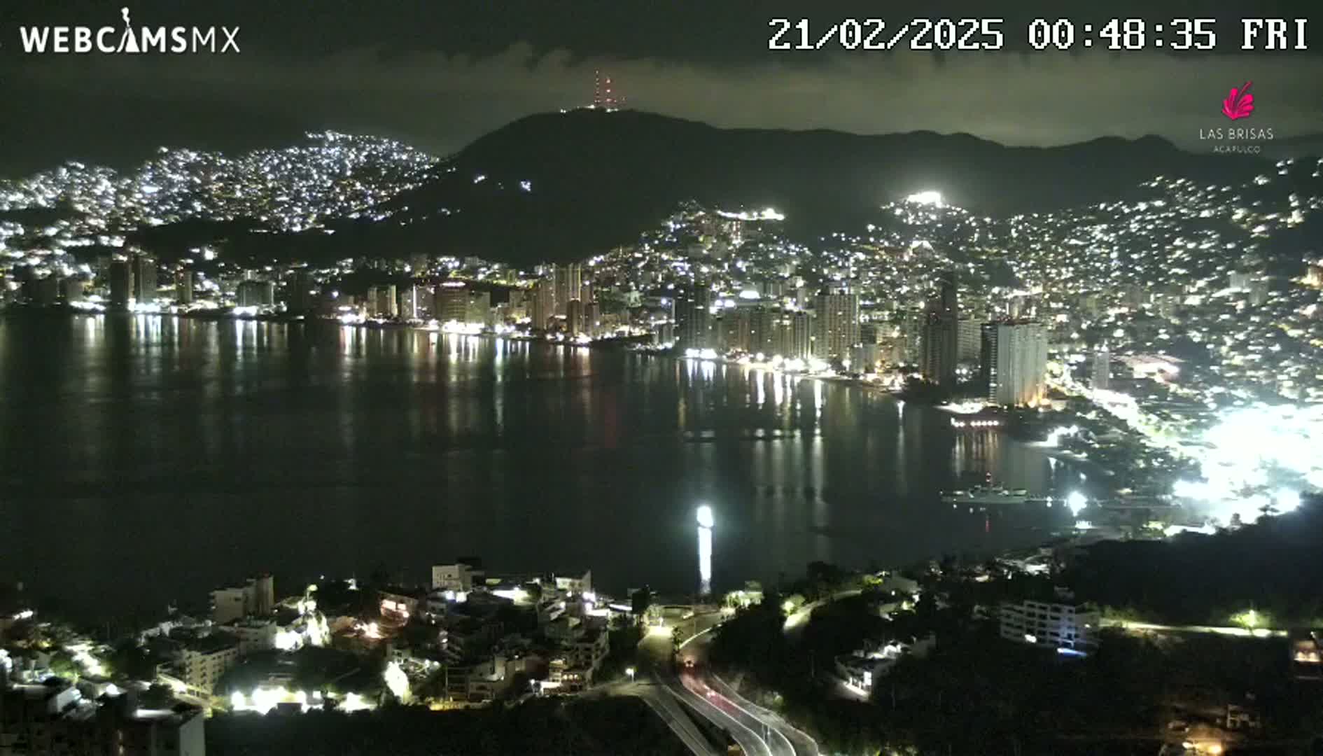 A nighttime view of a city sprawling across a hillside and along a bay, with its lights reflecting on the calm water.