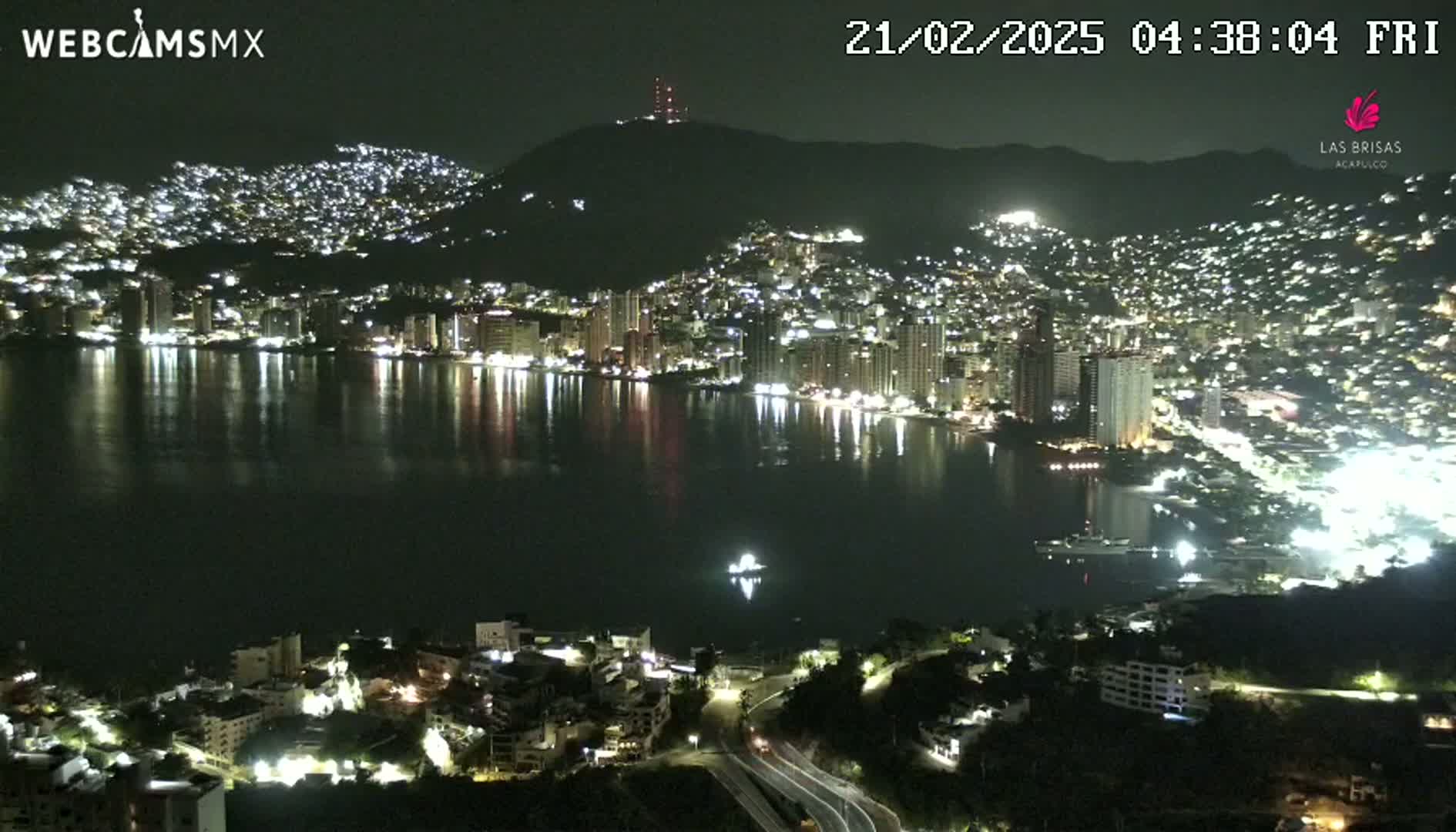 A nighttime view of a city sprawling across a hillside and along a bay, with its lights reflecting on the calm water.