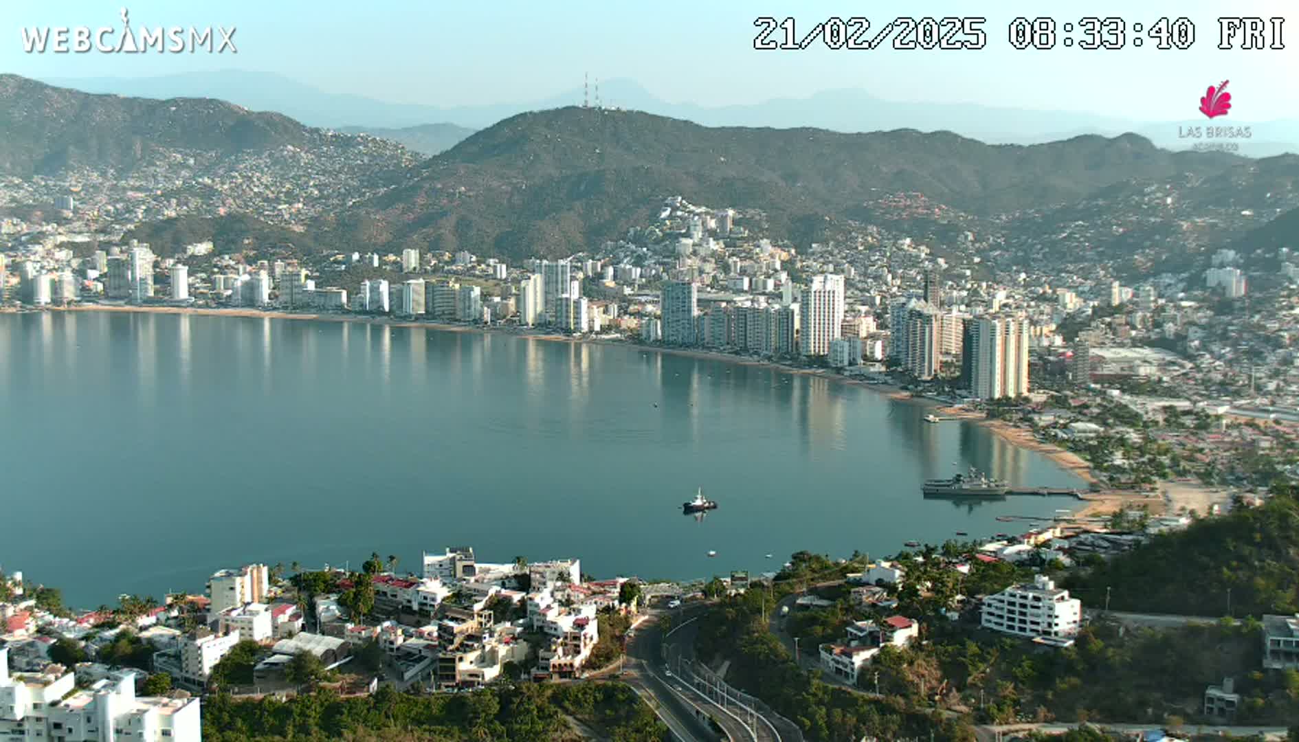 A coastal city with numerous high-rise buildings sprawls along a calm bay under a clear sky.