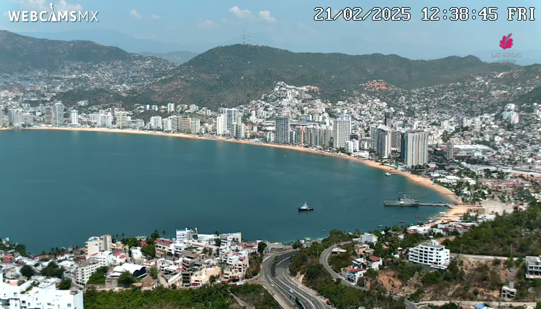 A coastal city with many high-rise buildings sits on a bay under a mostly sunny sky.