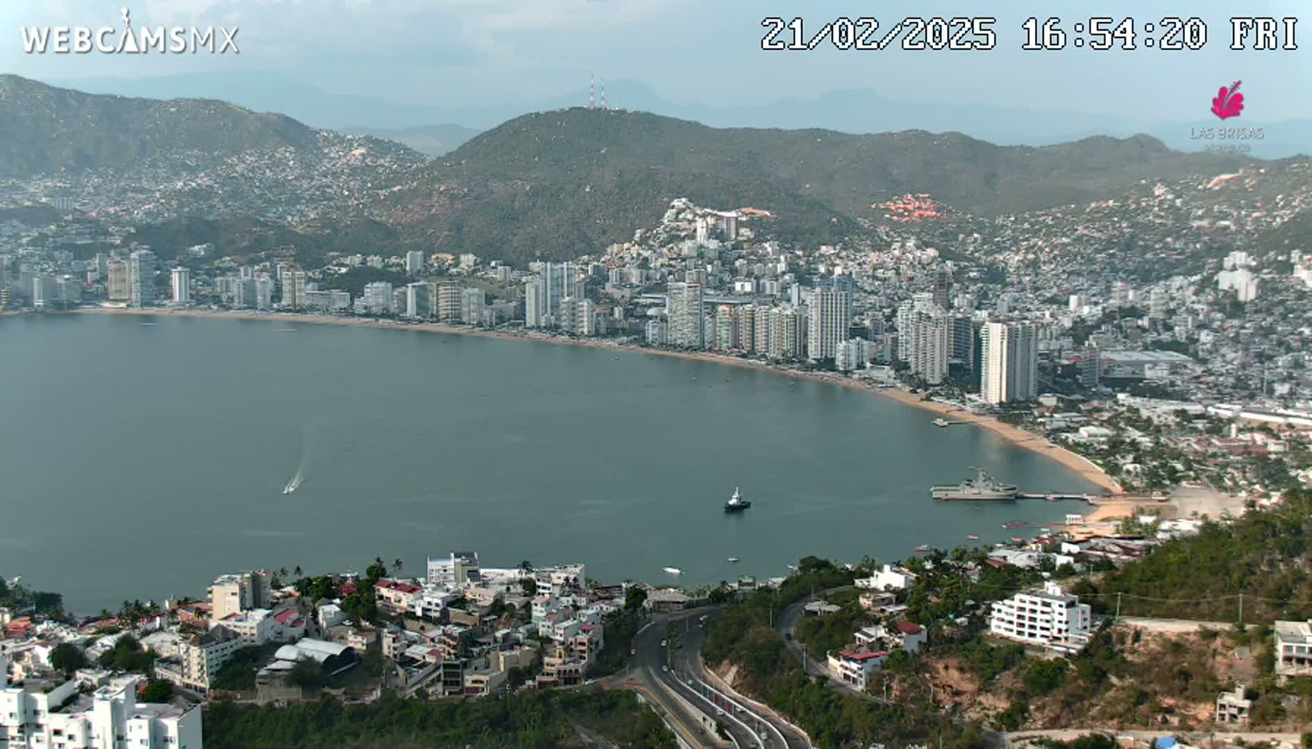 A coastal city with high-rise buildings along a bay, under partly sunny skies.