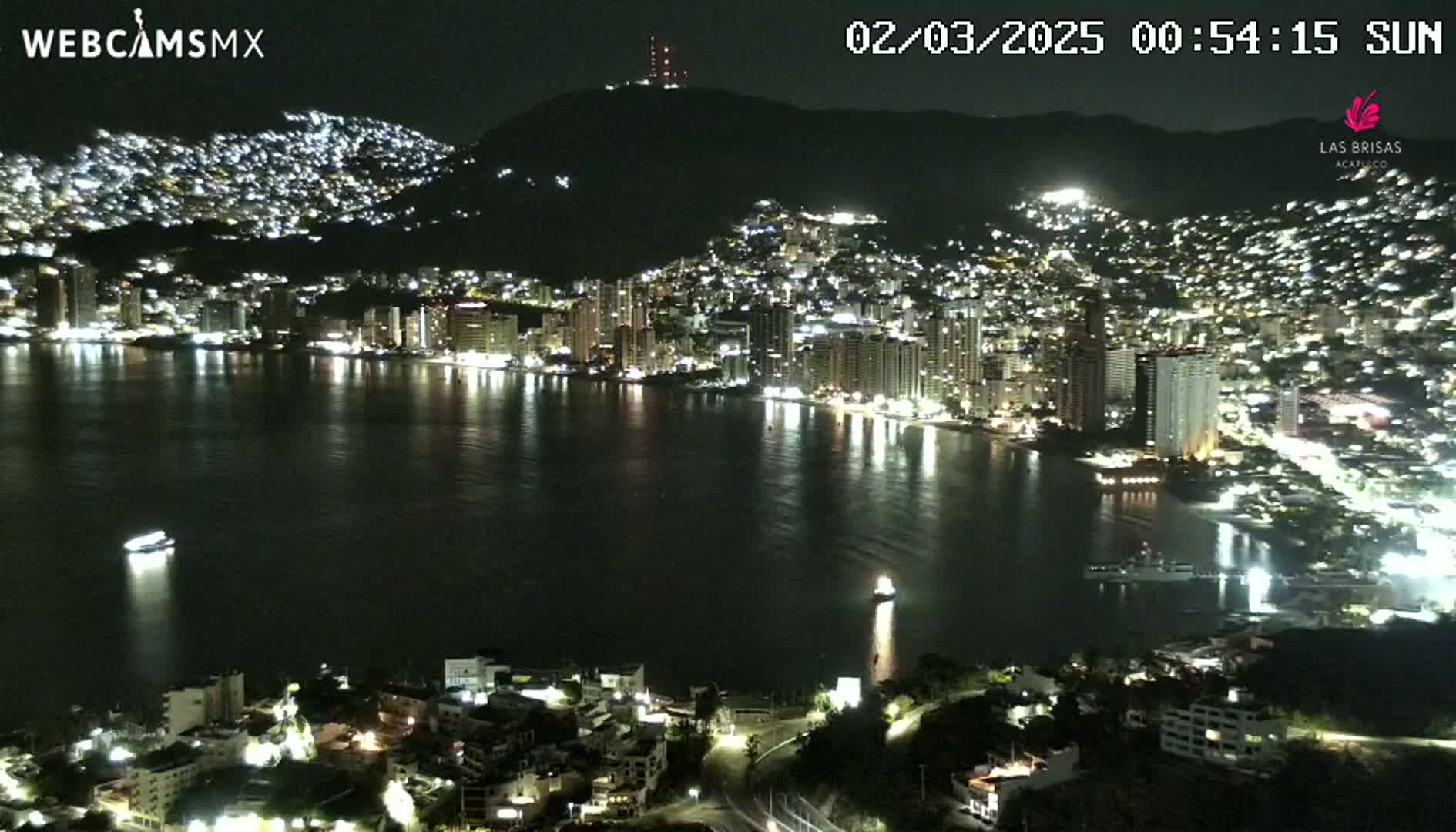 A nighttime view of a city on a hillside with its lights reflecting on a calm bay.