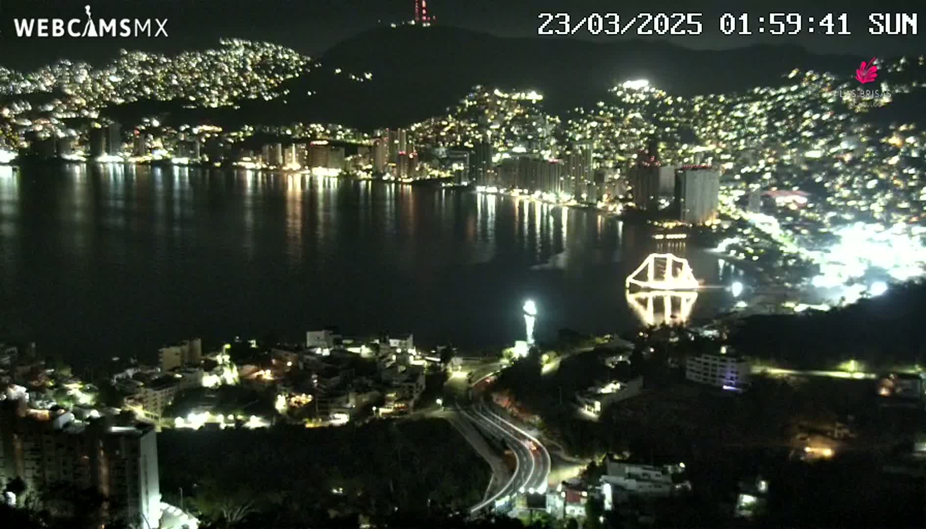 A nighttime view of a city sprawling along a bay, with its lights reflecting on the dark water.