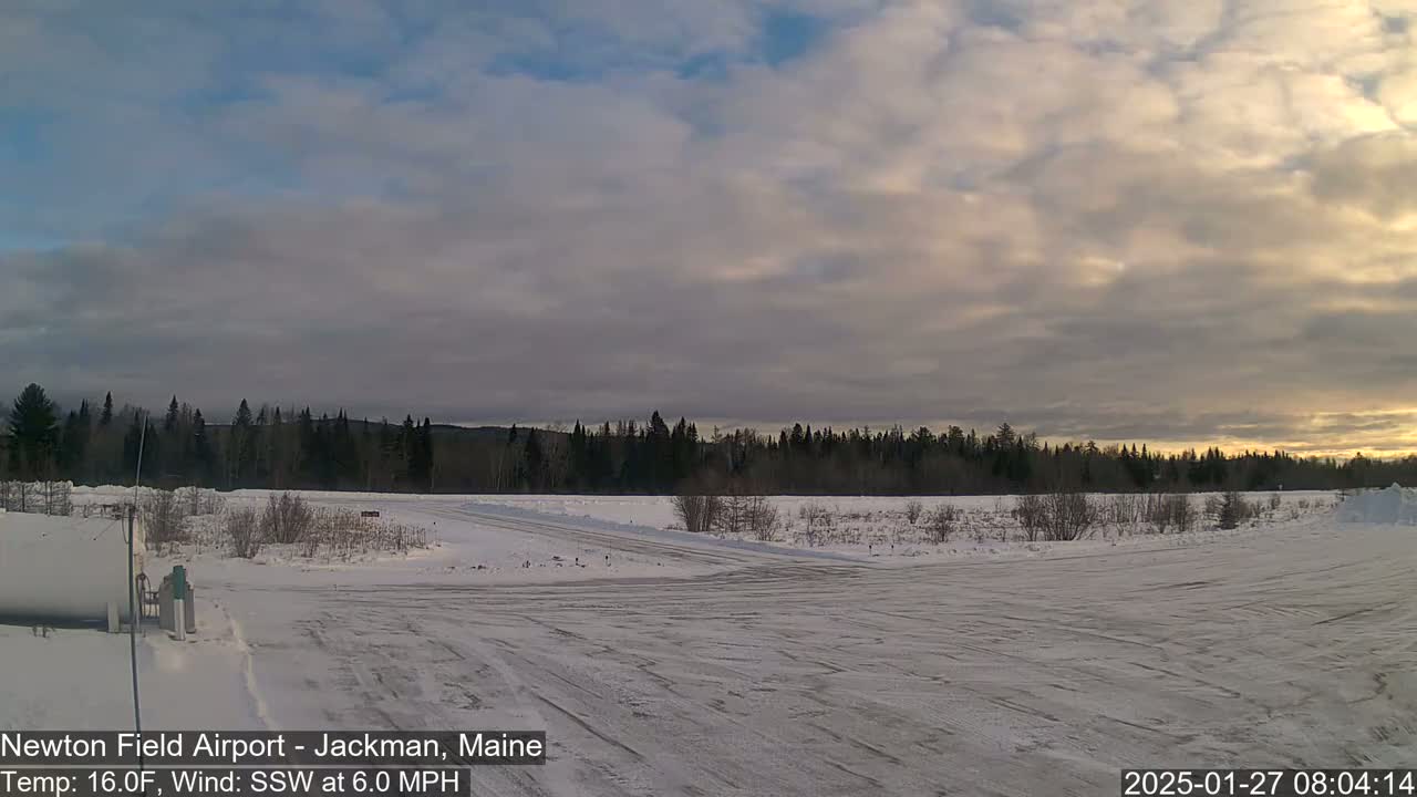 A snow-covered airfield with a line of dark trees in the background under a cloudy, partly sunny sky.