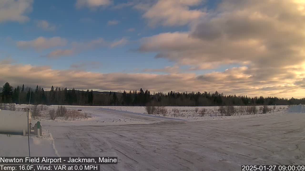 A snow-covered airfield is seen under a partly cloudy sky with a hint of pink in the clouds at sunrise.