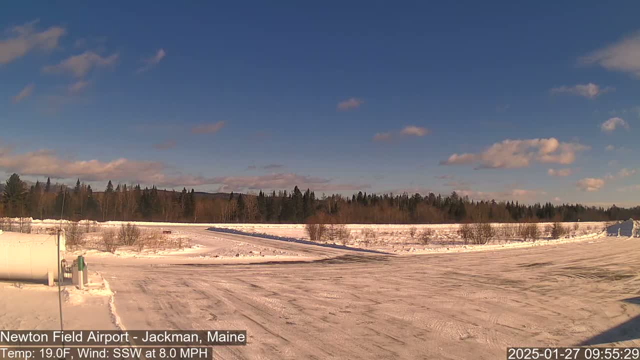 A snow-covered airfield with a line of trees in the background under a mostly clear, bright sky.