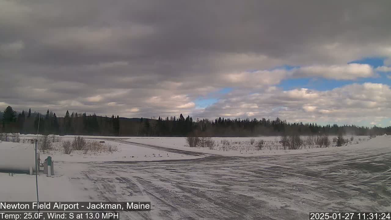A snow-covered airfield with a line of dark trees in the background under a partly cloudy sky.