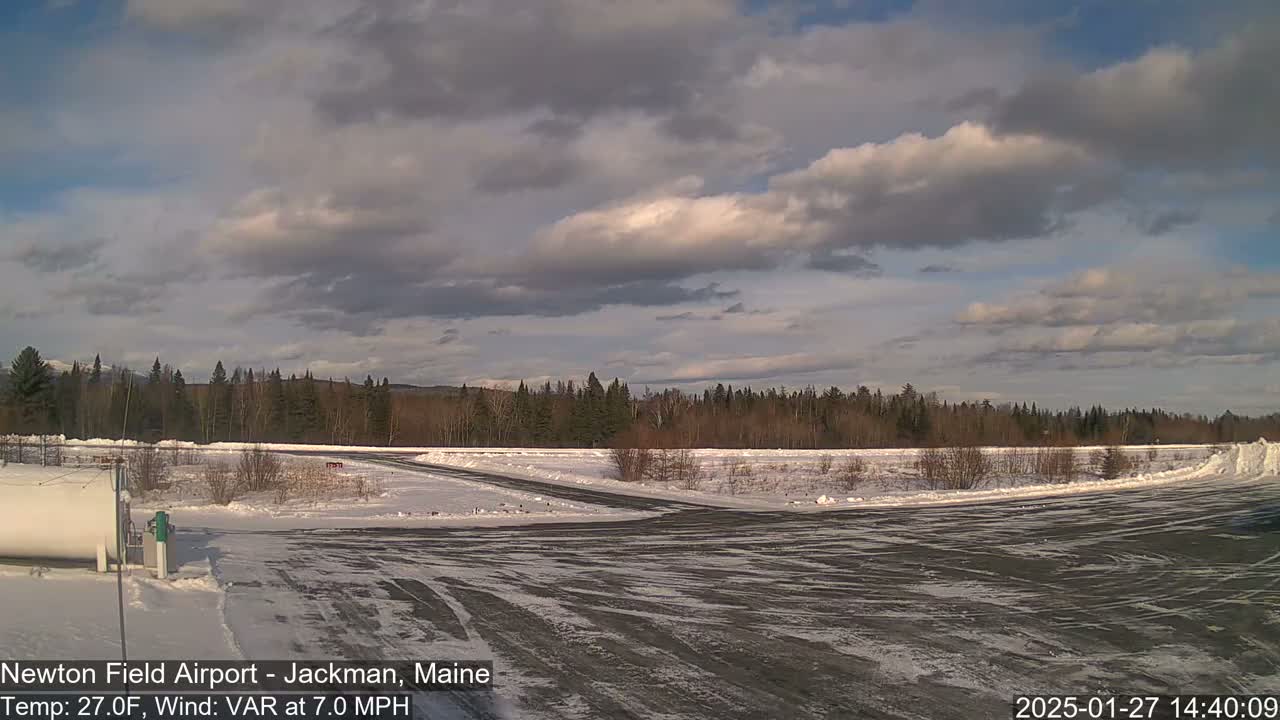 A snow-covered airfield is visible under a partly cloudy sky, with a line of trees in the background.
