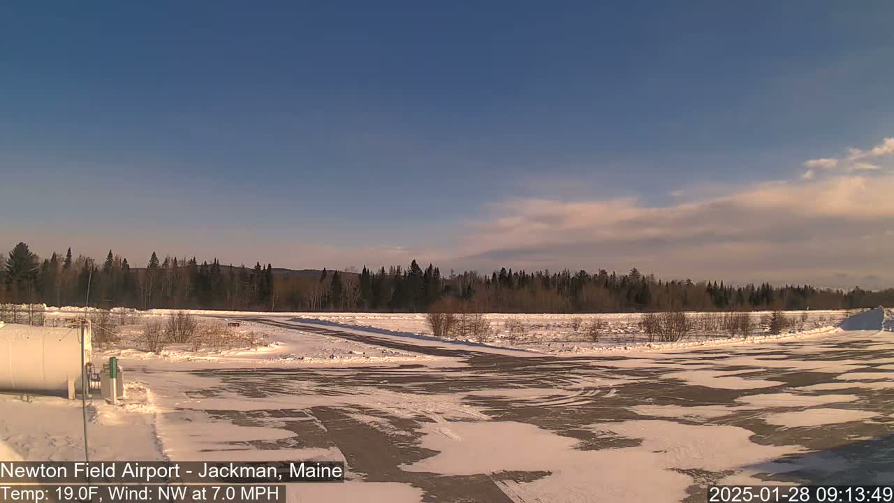 A snow-covered airfield with a mostly clear sky and a light northwest wind is visible, with a line of trees in the background.