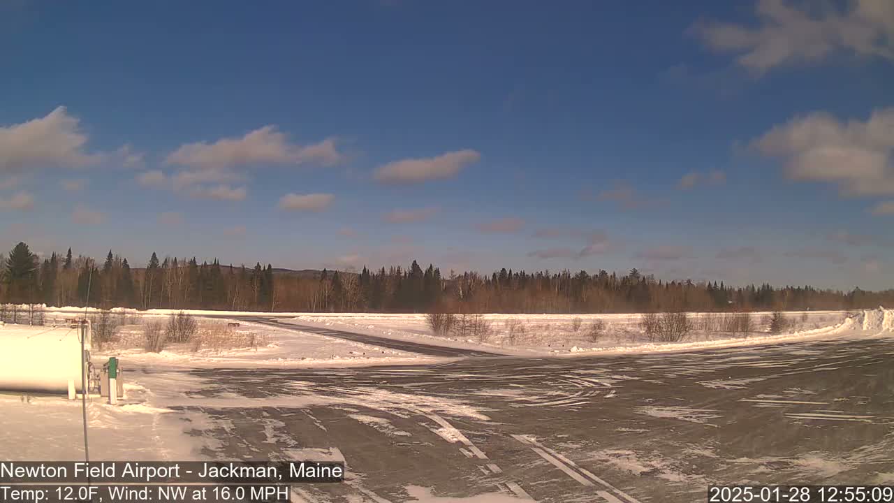 A snow-covered airfield with a line of trees in the background under a mostly clear, blue sky.
