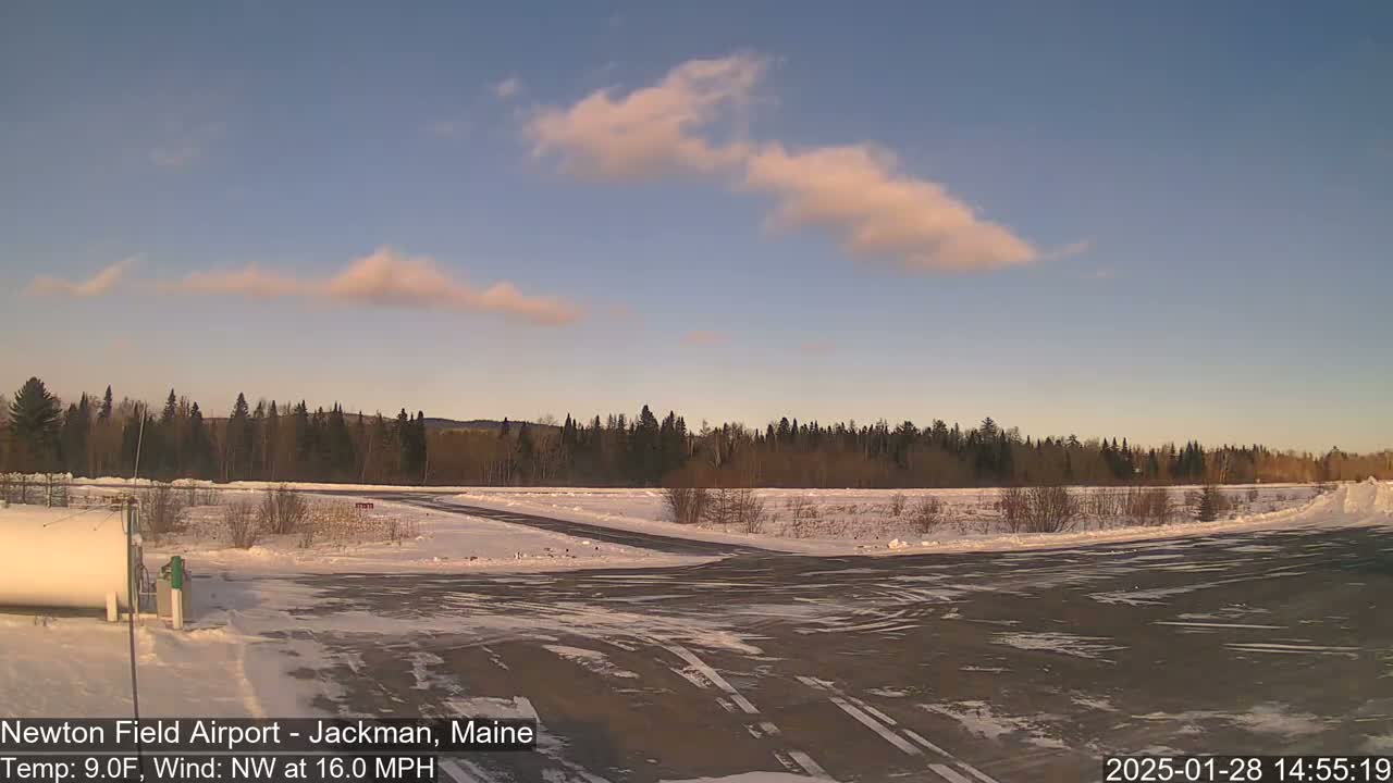 A snow-covered airfield with a line of trees in the background under a mostly clear sky with a few wispy clouds.