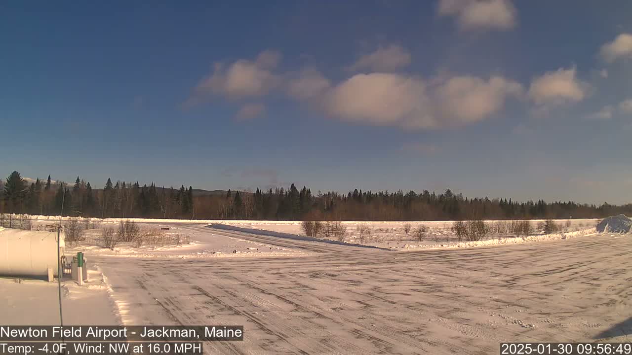 A snow-covered airfield with a treeline in the background under a partly cloudy sky.