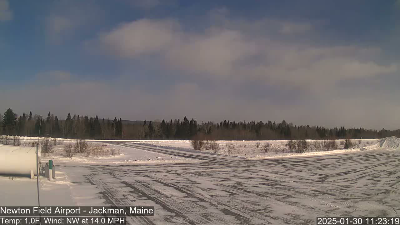 A snow-covered airfield with a line of trees in the background under a partly cloudy sky.