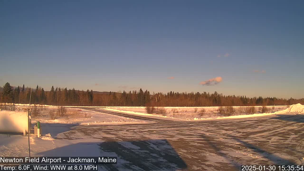 A snow-covered airfield with a line of trees in the background under a clear, light blue sky.