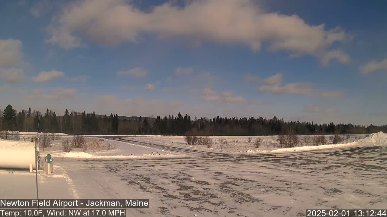 A snow-covered airfield with a line of trees in the background under a partly cloudy sky.