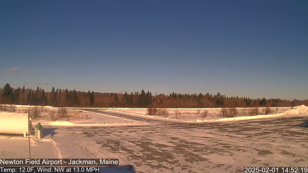 A snow-covered airfield with a line of trees in the background under a clear blue sky.