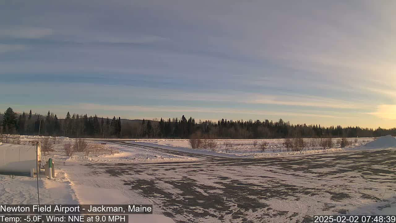 A snow-covered airfield is visible with a line of trees in the background under a partly cloudy sky.