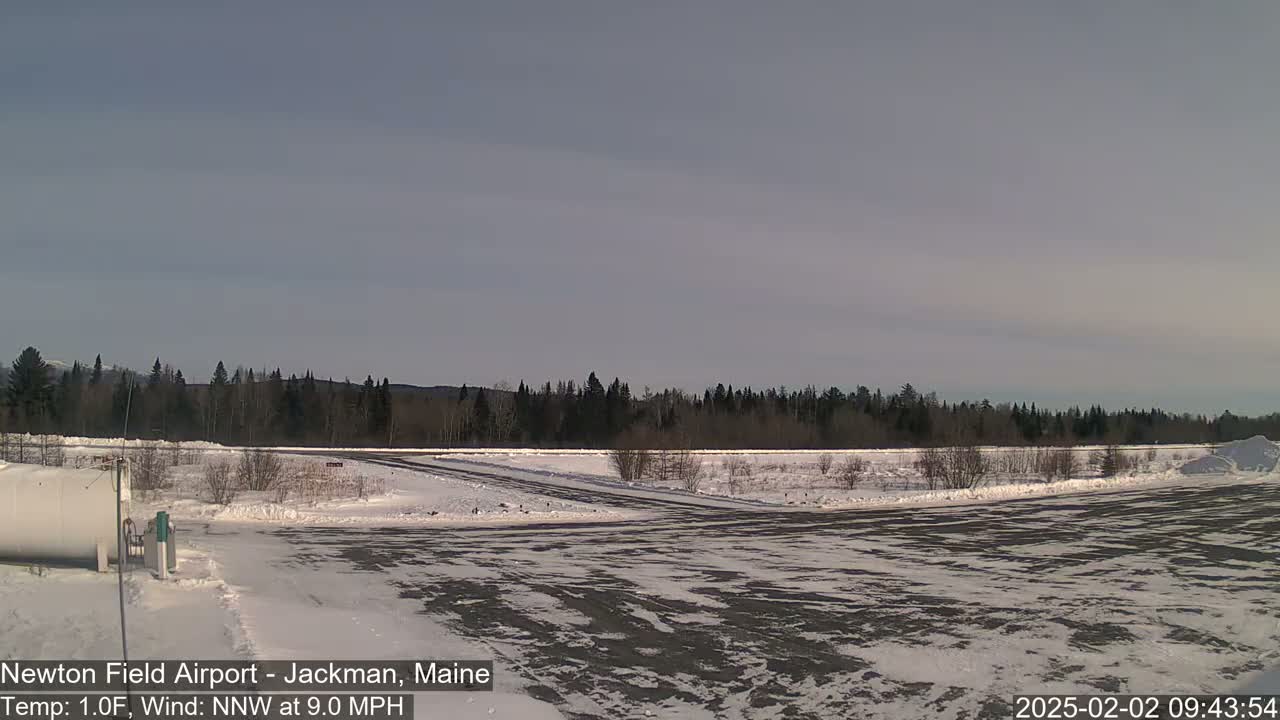 A snow-covered airfield with a line of trees in the background under a mostly clear sky.