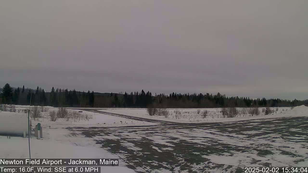 A snow-covered airfield is shown under an overcast sky, with a line of dark trees in the background.