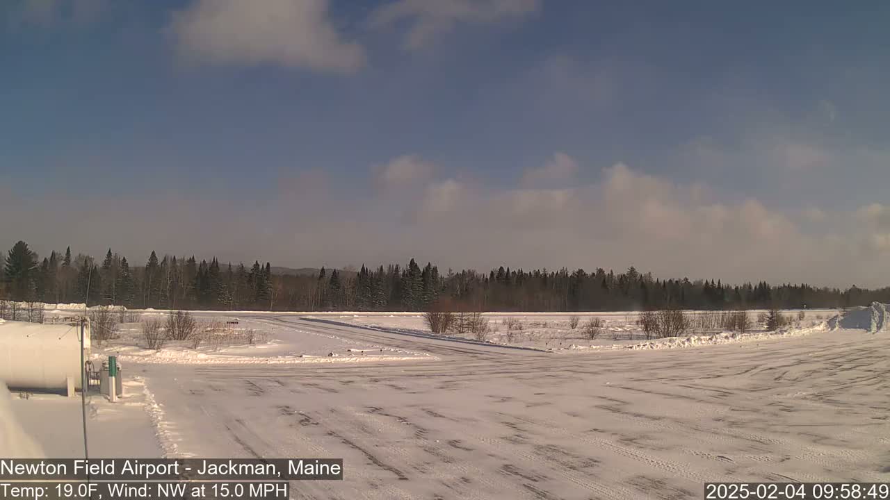 A snow-covered airfield with a line of evergreen trees in the background under a partly cloudy sky.