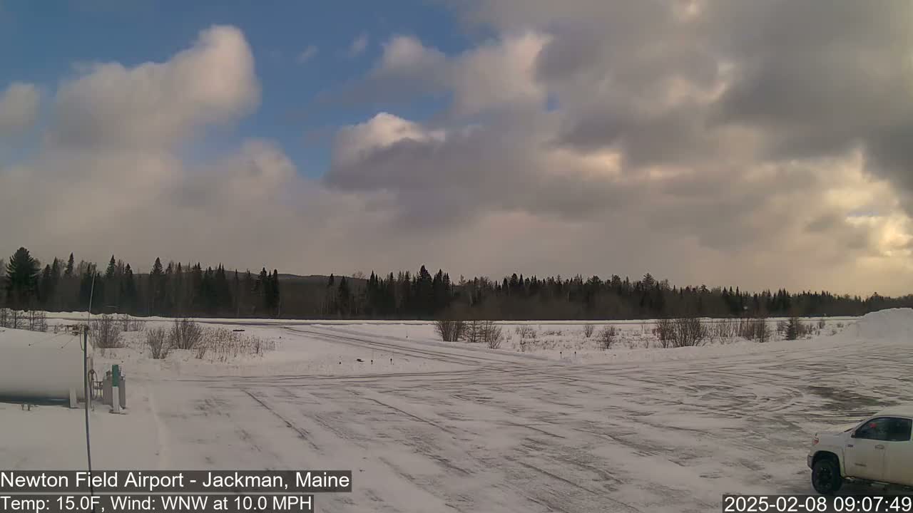 A snow-covered airfield with a line of dark trees in the background under a partly cloudy sky.