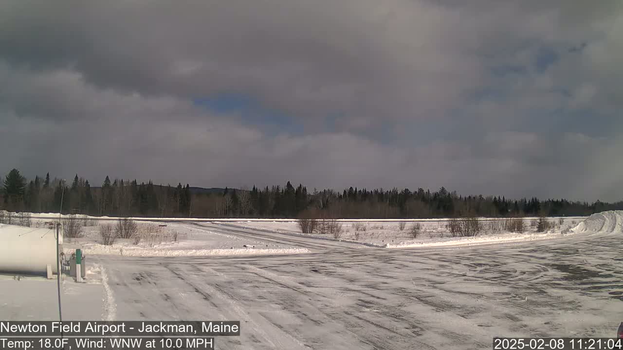 A snow-covered airfield with a line of trees in the background under a mostly cloudy sky.