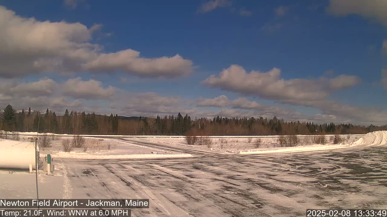A snow-covered airfield with a line of trees in the background under a partly cloudy blue sky.