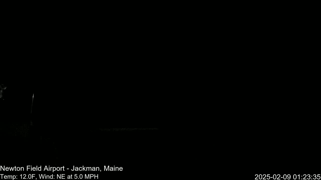 A dark, nighttime scene shows a mostly black field with a faint, thin, vertical line of light in the distance under a clear, dark sky.