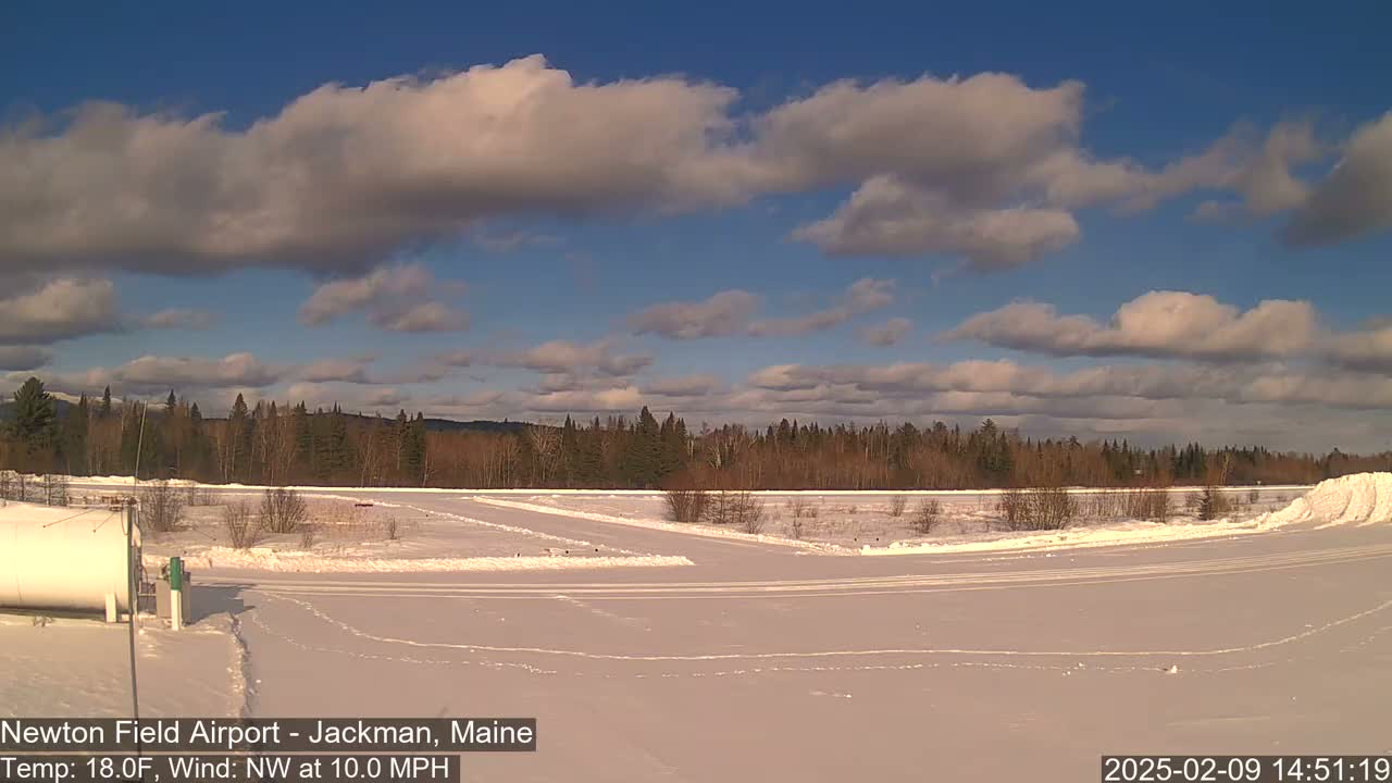 A snow-covered airfield with a line of trees in the background under a partly cloudy blue sky.