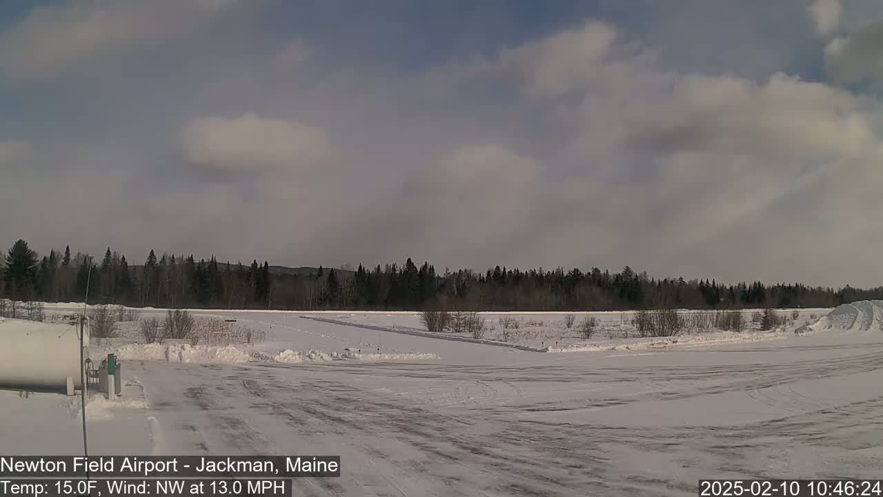 A snow-covered airfield with a line of trees in the background under a partly cloudy sky.