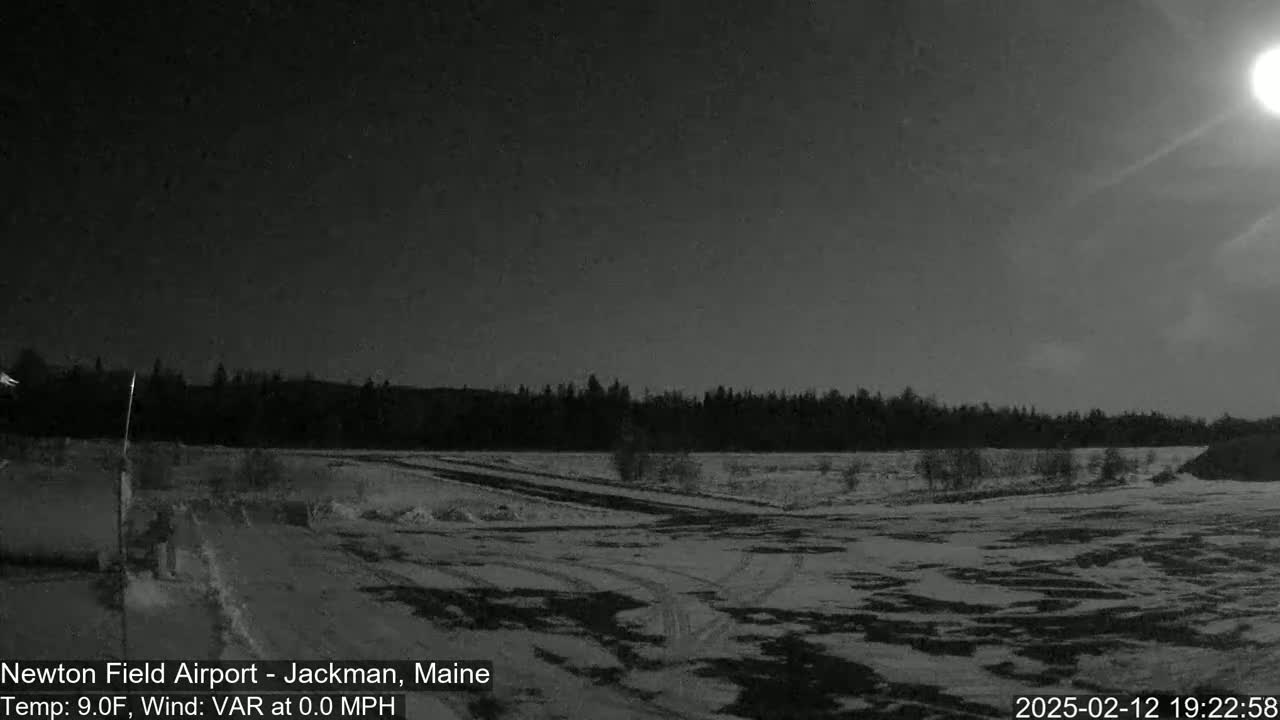 A snow-covered field is visible under a mostly clear night sky with a bright moon, in front of a dark treeline.