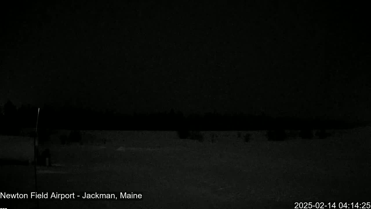 A nighttime, snow-covered landscape is visible, showing a dark sky, a line of trees in the distance, and a sparsely lit area in the foreground.