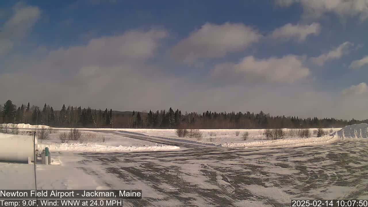 A snow-covered airfield with a coniferous forest in the background under a partly cloudy sky.