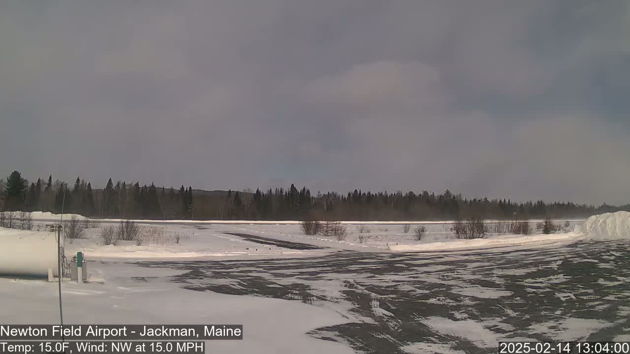 A snow-covered airfield with a line of dark trees in the background under a mostly cloudy sky.