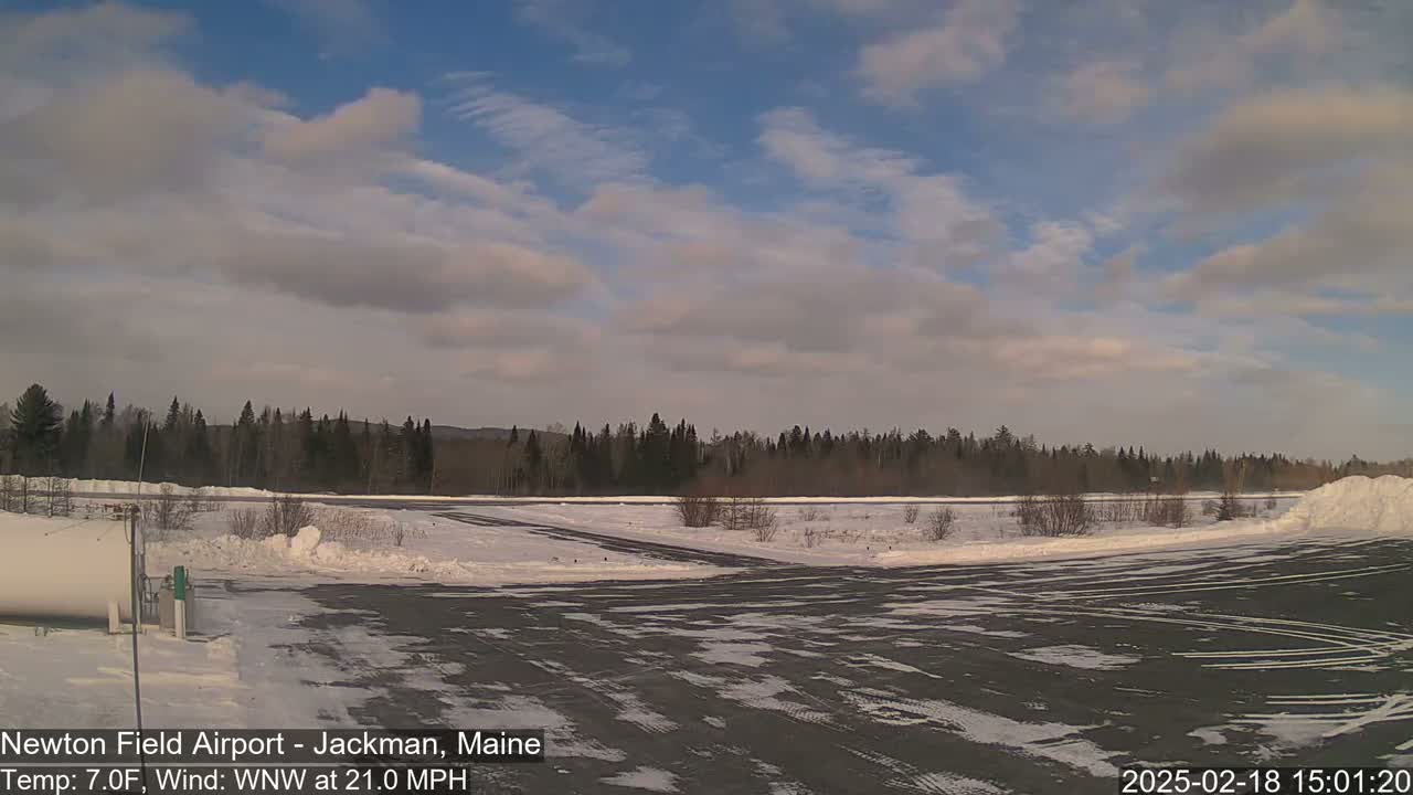 A snow-covered airfield with a line of trees in the background under a partly cloudy sky.