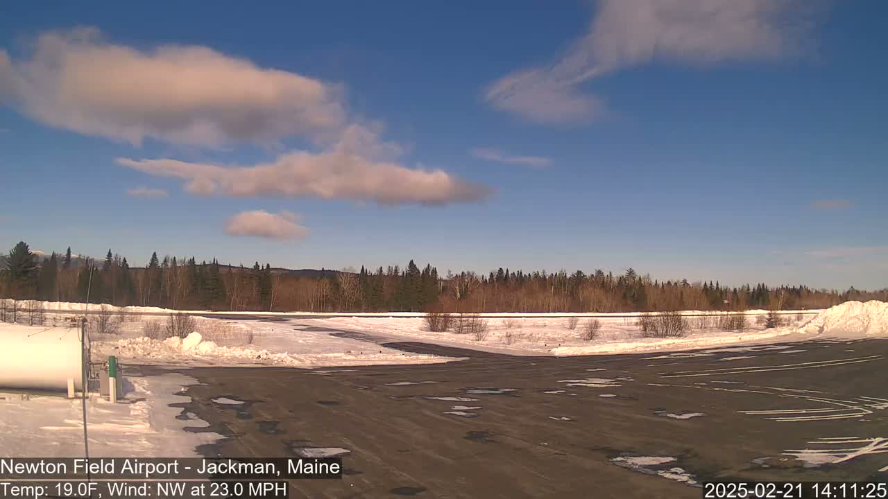 A snow-covered airfield with a few scattered clouds under a mostly clear blue sky.